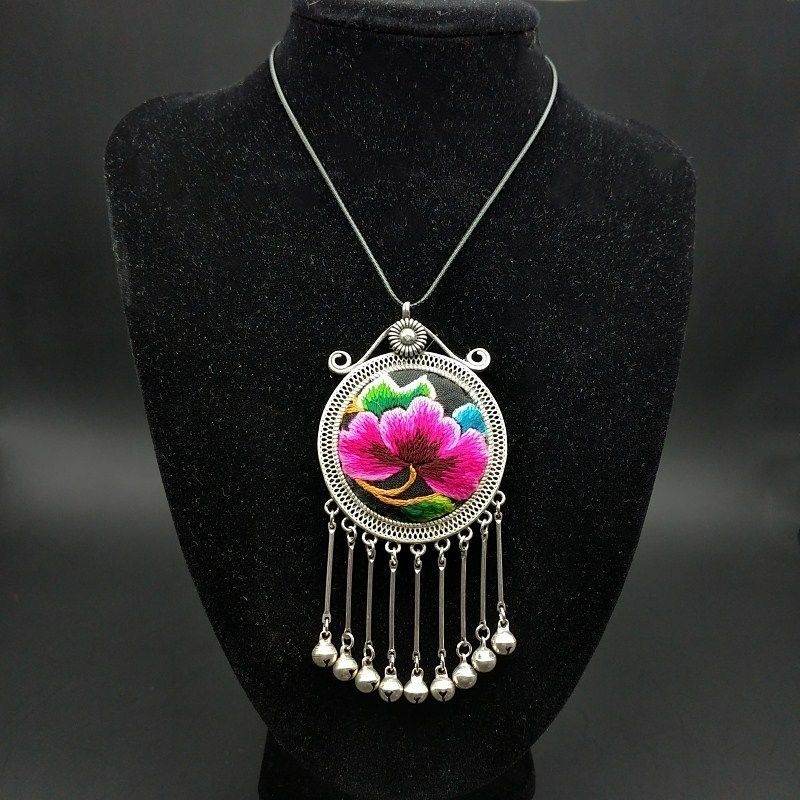 Silver pendant on a bust with a pink embroidered flower and hanging bells
