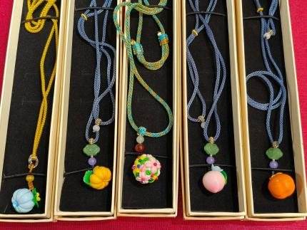 Five cords with small pendants shaped like a peach, an orange and a pumpkin, laid in boxes