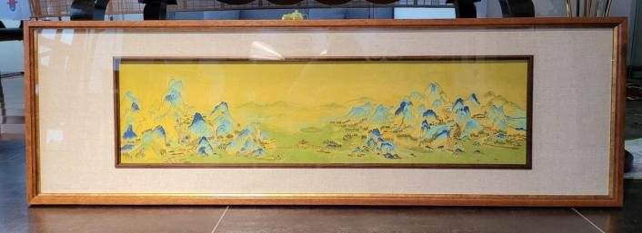 A framed panel of blue-green mountains on a yellow ground