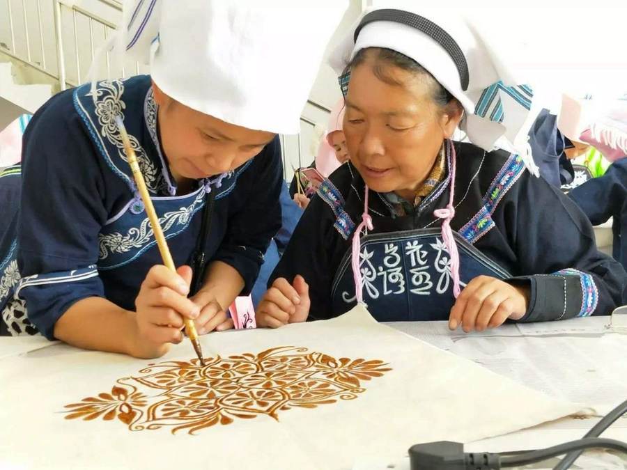 Two makers painting a pattern in amber resist onto white cloth