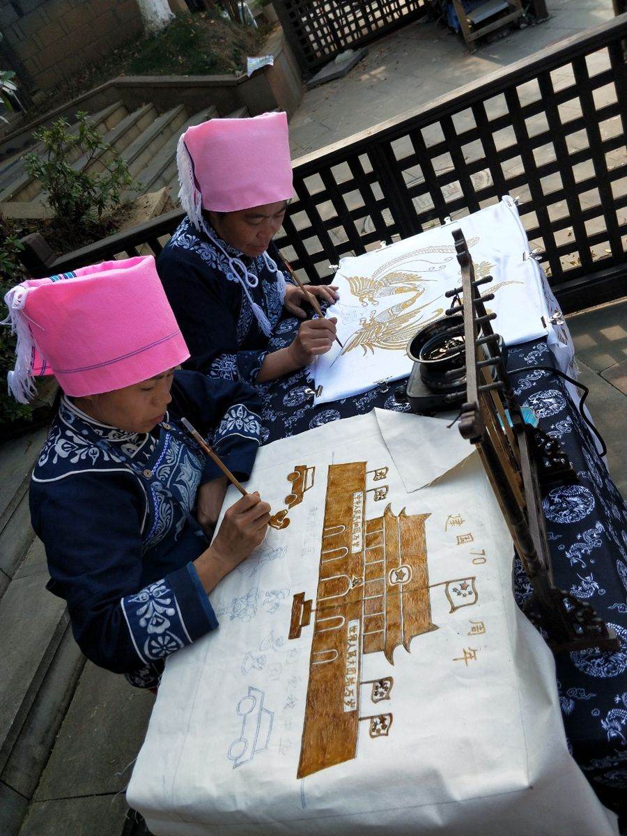 Two makers seated at a table painting cloth outdoors