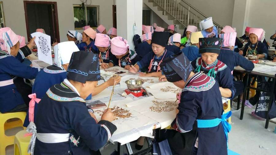A workshop room filled with makers painting cloth at long tables