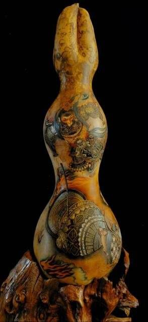 A double gourd on a root stand, burned with figures and patterns, against a black background