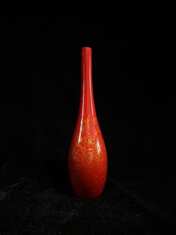 A tall red lacquer vase against a black background