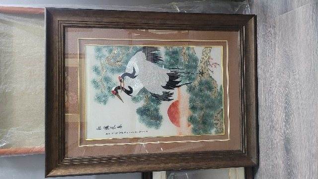 A framed embroidery of two cranes under a pine with a red sun