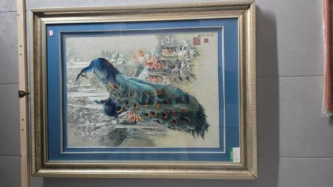 A framed embroidery of a peacock with a fine blue-green tail