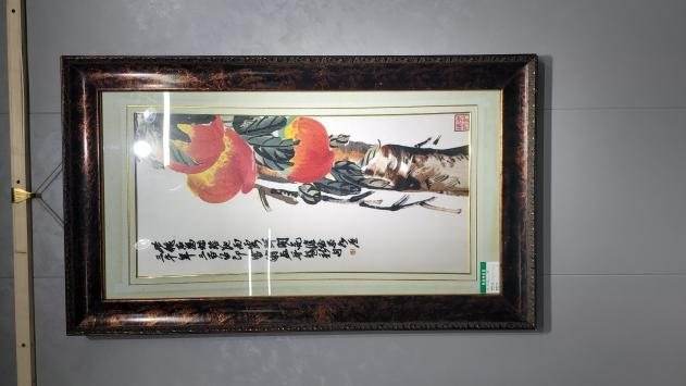 A framed embroidery of red peaches on a branch, with calligraphy