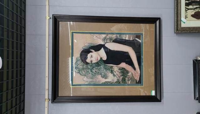 A framed embroidered portrait of a seated woman in a black dress